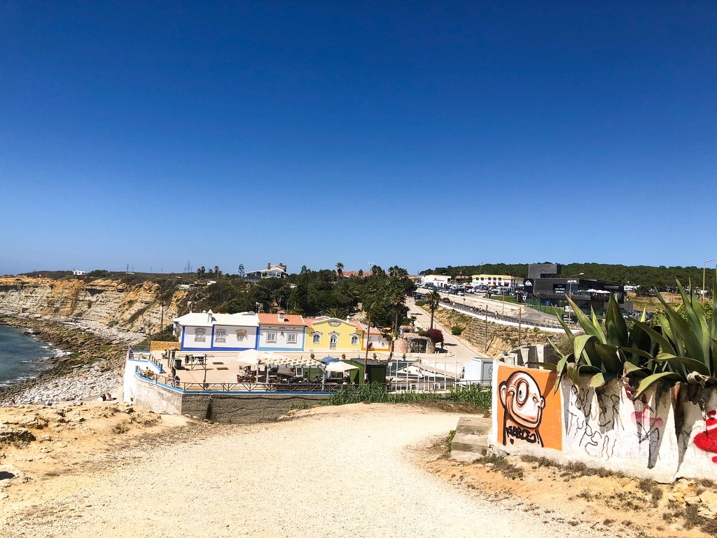 The stone path down to Praia do Matadouro with white and yellow buildings in the background and colorful graffiti in the foreground